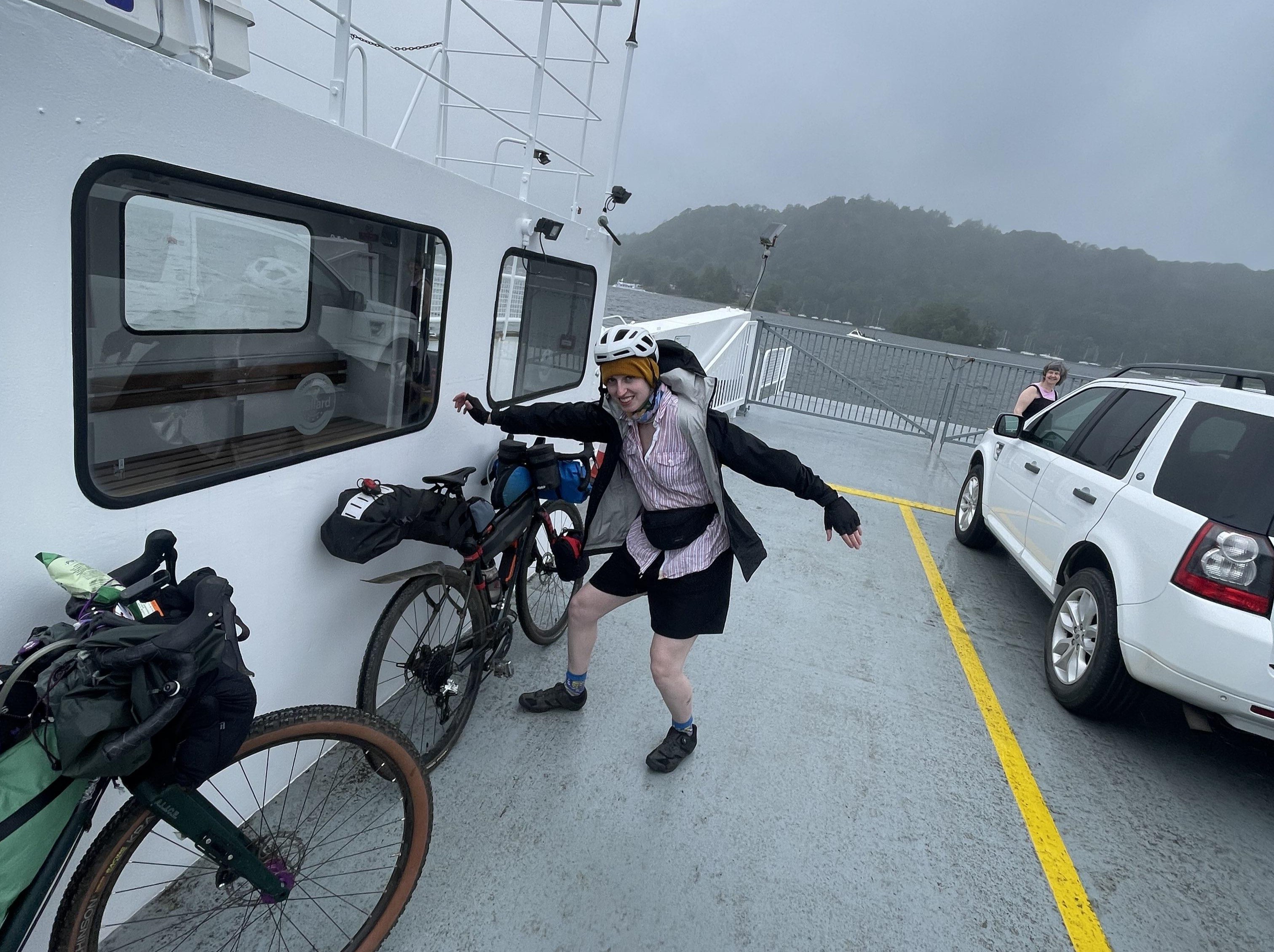 A photo of me striking a silly pose next to my bike while on the ferry across Lake Windermere.